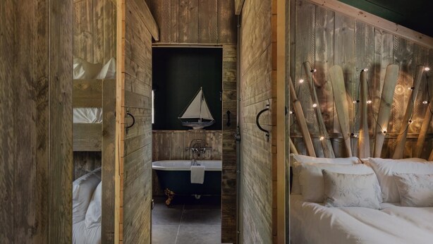 A rustic wooden room with a bed, a small sailboat decoration, and a bathroom with a bathtub. - 3 Bed in Hintlesham (oc-r39060) (Hintlesham)