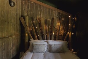 Une pièce en bois avec un lit, des guirlandes lumineuses et un luminaire fixé au mur.