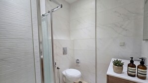 Een moderne badkamer met een glazen douchecabine, toilet, wastafel met houten onderkast en twee flesjes Aesop op het aanrecht.