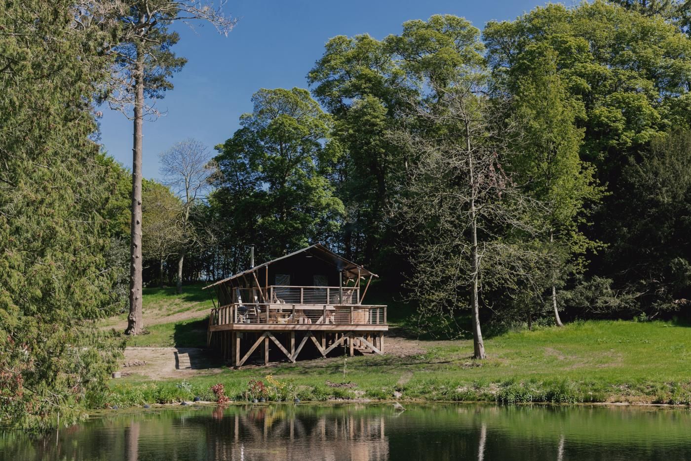 A wooden cabin with a deck, surrounded by trees and a body of water.