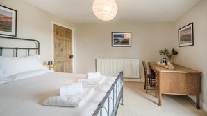 Ein Schlafzimmer mit Bett, Nachttisch, Schreibtisch, Stuhl, Heizkörper und einer Pendelleuchte.