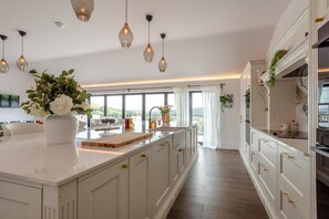 A modern kitchen with a large island, pendant lights, and a view of the outdoors. - 4 Bed in Bishops Tawton (oc-s35786) (Bishop's Tawton)