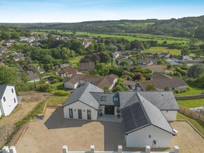 A residential area with houses, a large white building with a sloped roof, and a view of a green valley. - 4 Bed in Bishops Tawton (oc-s35786) (Bishop's Tawton)