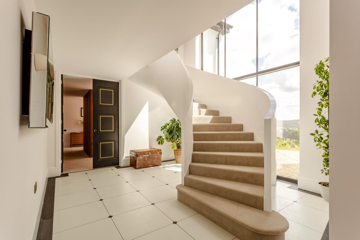 A modern interior with a spiral staircase, a large window, and a door leading to another room.