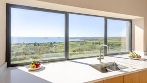 A kitchen with a large window, a sink, and a bowl of fruit. - 5 Bed in Mynytho (oc-t39070) (Mynytho)