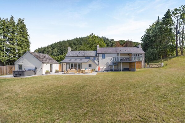 A two-story house with a balcony, a patio with outdoor furniture, and a fenced yard.