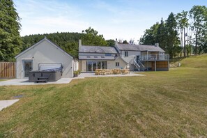 A two-story house with a patio area, a hot tub, and a deck.