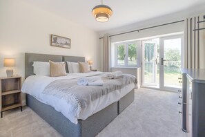 A bedroom with a large bed, bedside tables, a lamp, a painting, and a sliding glass door leading to a balcony.