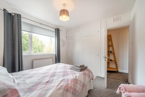 A bedroom with a bed, a radiator, a window with curtains, a door leading to another room, and a small ladder. - 3 Bed in Auldgirth (oc-g38241) (Auldgirth)