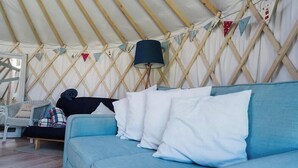 Interior de una yurta con sofá, almohadas, lámpara y una silla.