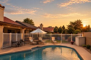 A swimming pool with a white fence, lounge chairs, and a patio area. - Desert Disconnect | Pool • Putting Green (Gilbert)