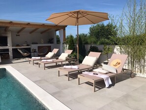 Ein Poolbereich mit Liegestühlen, einer Pergola und einem großen Sonnenschirm.