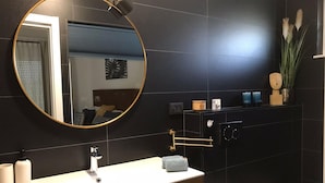 A modern bathroom with a round mirror, a white sink, a toilet, and a dark tiled wall. - Comfortable Family Retreat With Pool (Vodnjan)