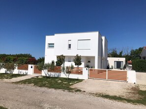 Ein modernes, zweistöckiges Haus mit flachem Dach, einer kleinen Veranda und einem eingezäunten Garten.