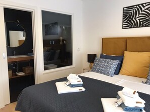 Ein Hotelzimmer mit Bett, Nachttisch, Fenster und einem durch die Tür einsehbaren Badezimmer.