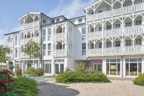 A white building with multiple balconies and large windows, surrounded by greenery and a gravel path. - Ostseeurlaub - Strandnahe Ferienwohnung mit Balkon in Sellin (Sellin)