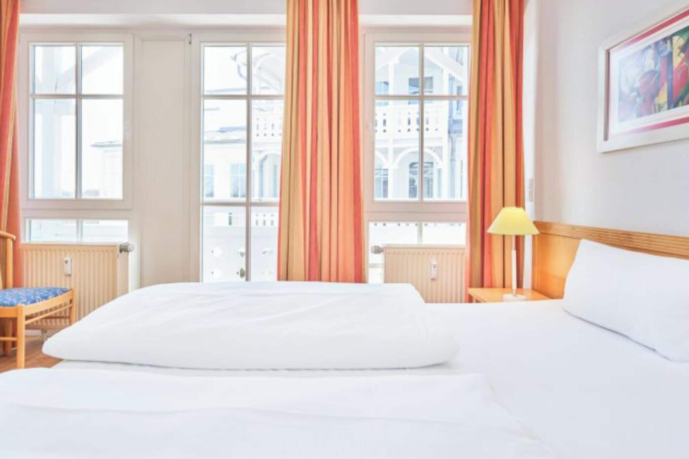 Une chambre d’hôtel avec un grand lit, une chaise, une table de chevet avec une lampe et une vue sur les bâtiments par les fenêtres.