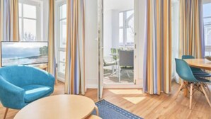 A modern hotel room with a large window, a blue armchair, a round table, and a dining area with chairs. - Komfortable Ferienwohnung fur bis zu 4 Personen (Sellin)