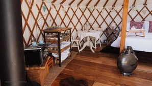A cozy interior of a yurt with a wooden table, chairs, a bed, and a large vase.