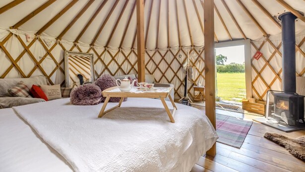 A cozy yurt interior with a bed, a table with tea set, a fireplace, and a view of the outdoors. - 1 Bed in Bronington (oc-d39075) (Bronington)