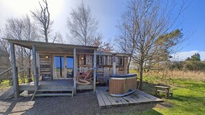 Un chalet rustique en bois doté d’un bain à remous, d’un espace salon extérieur et d’une véranda couverte.