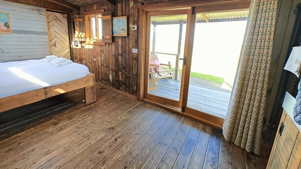 Une pièce de cabane en bois comprenant un lit, une chaise et une porte-fenêtre coulissante donnant sur un espace extérieur.