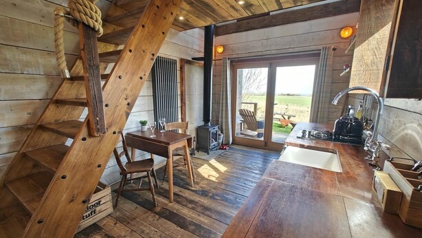 A rustic interior with a wooden staircase, a dining area, a kitchen, and a sliding glass door leading to an outdoor deck. - 1 Bed in Earsdon (oc-l40253) (Earsdon)
