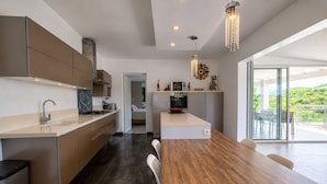 A modern kitchen with a dining area, a view of greenery, and a large window.