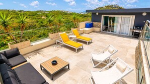 A rooftop terrace with outdoor furniture, a barbecue area, and a view of a green landscape.
