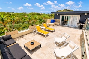 A rooftop terrace with outdoor furniture, a barbecue area, and a view of a green landscape.