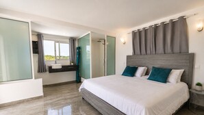 A modern bedroom with a large bed, a built-in bench, a small bedside table, and a view of the outdoors.