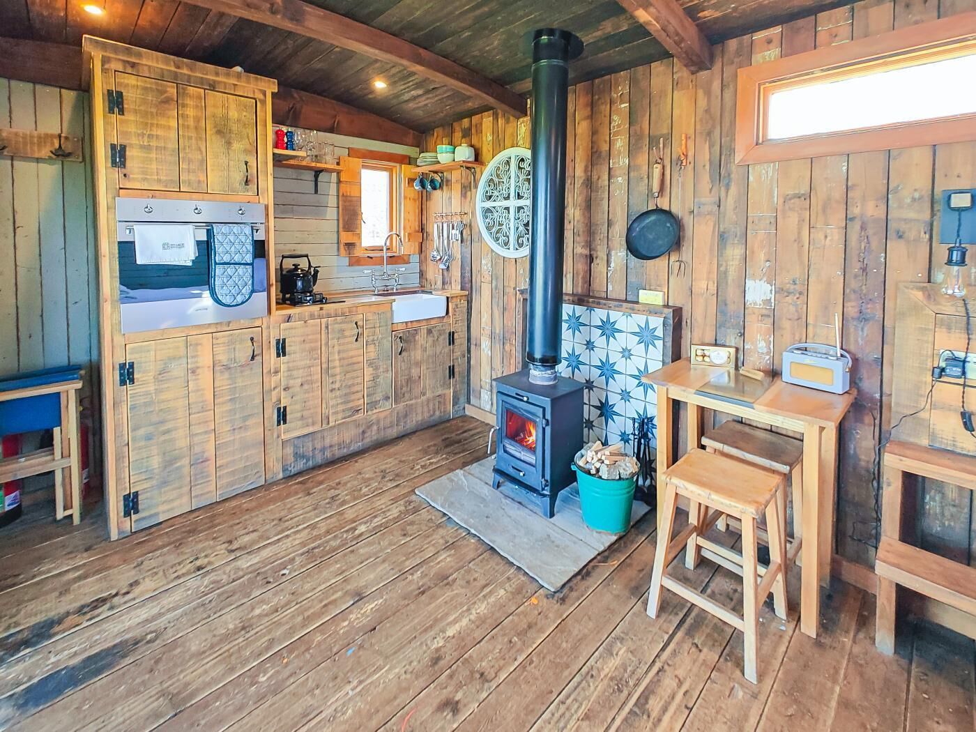 A rustic kitchen with wooden cabinets, a wood-burning stove, a radio, and a tiled backsplash.