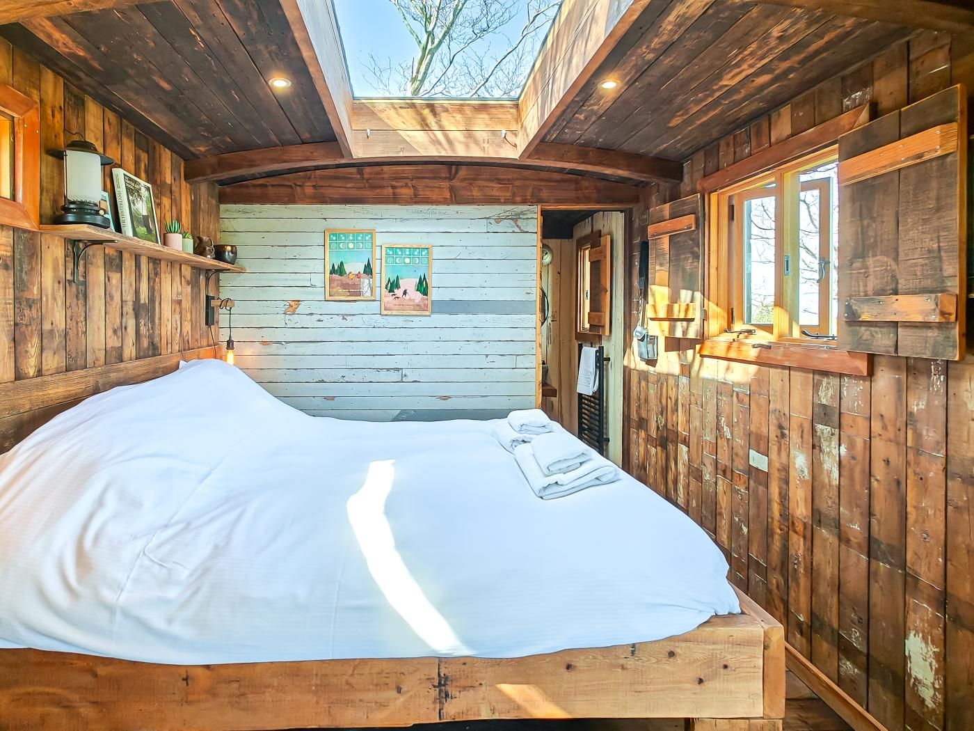 A wooden cabin with a loft-style bed, wooden walls, and a skylight.