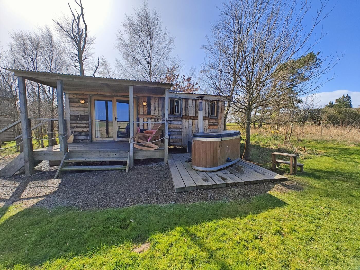Een rustieke houten chalet met een bubbelbad, buitenzitplaatsen en een overdekt terras.