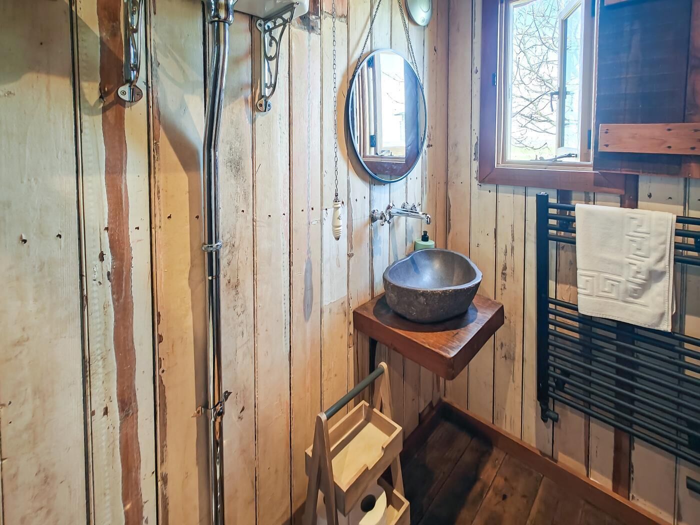 A rustic bathroom with wooden walls, a metal sink, a mirror, and a towel rack.