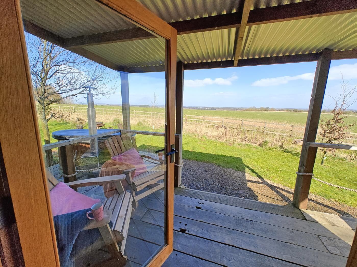 Une terrasse en bois avec une porte vitrée donnant sur un champ herbeux.
