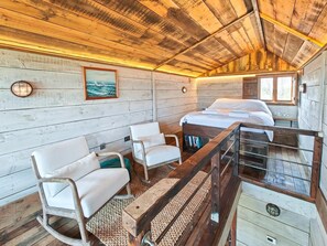 A cabin interior with a bed, two white chairs, a wooden rocking chair, a small table, and a window with a view of the outdoors. - 1 Bed in Earsdon (oc-l40253) (Earsdon)