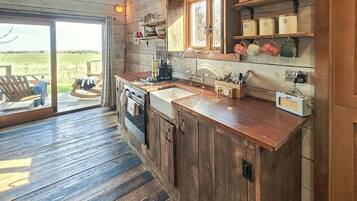 A rustic kitchen with wooden cabinets, a built-in oven, a sink, and a window overlooking a deck.