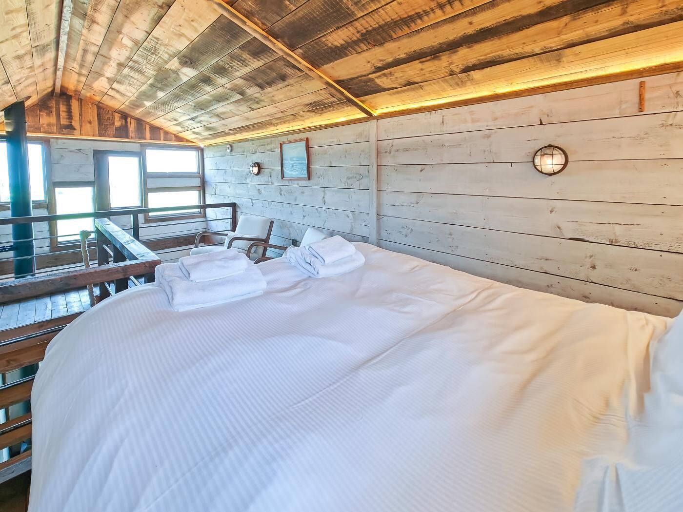 A wooden cabin-style room with a bed, a chair, and a window.