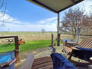 A covered outdoor seating area with wooden benches and a picnic table, overlooking a grassy field and a tree. - 1 Bed in Earsdon (oc-l40253) (Earsdon)