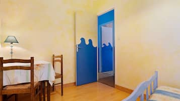 A room with a wooden bed, a table with chairs, a lamp, and a blue door with a wave design.