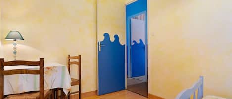 Una habitación con una cama de madera, una mesa con sillas, una lámpara y una puerta azul con un diseño de olas.