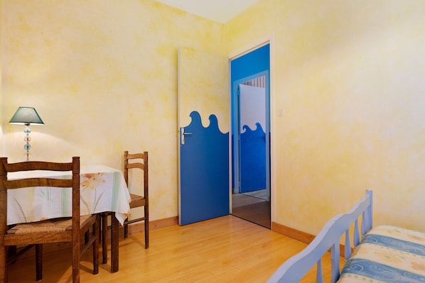 Une pièce avec un lit en bois, une table avec des chaises, une lampe et une porte bleue ornée d’un motif ondulé.