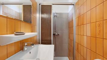 Une salle de bain avec un lavabo blanc, un miroir, une douche et des murs recouverts de carreaux orange.