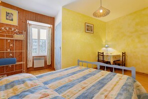 A bedroom with a bed, a desk with a chair, a window with curtains, and a hanging light fixture.