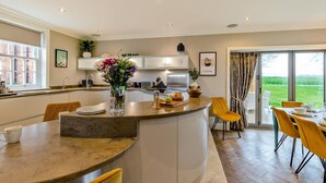 A modern kitchen with a central island, dining area with yellow chairs, and a large sliding glass door to a garden. - 5 Bed in Weeton (oc-p39054) (Weeton-with-Preese)