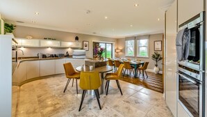 A modern kitchen with a central island, dining area with yellow chairs, and a built-in oven. - 5 Bed in Weeton (oc-p39054) (Weeton-with-Preese)