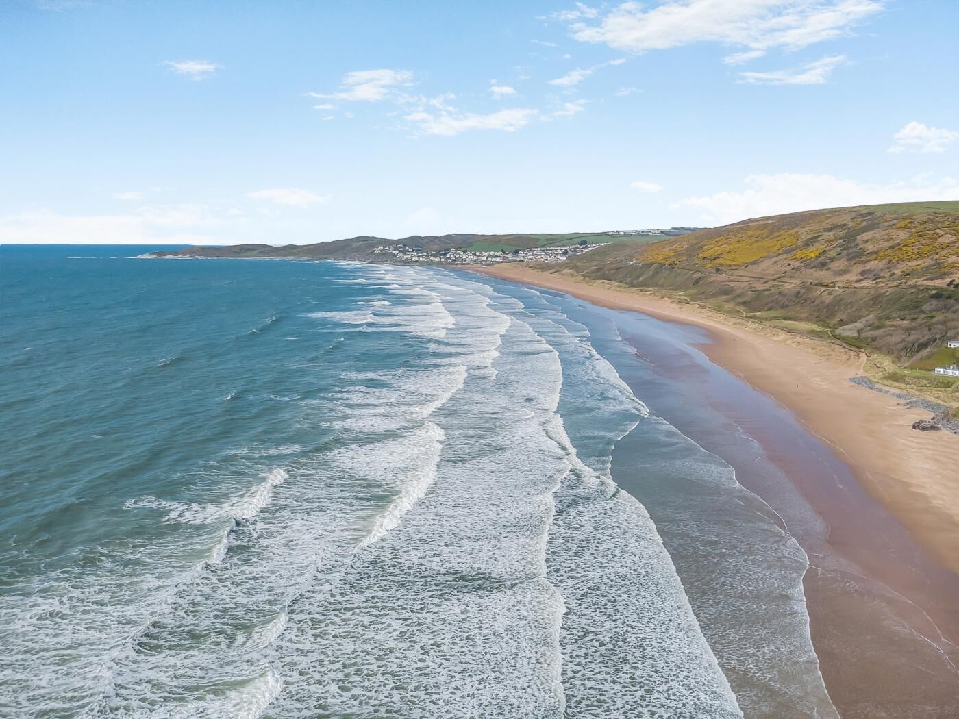 A coastal beach with waves, a sandy shore, and distant buildings.