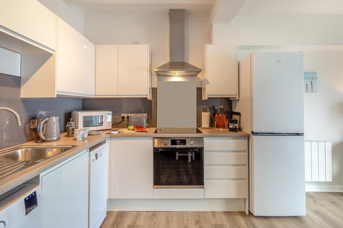 A modern kitchen with white cabinets, a stainless steel sink, a microwave, toaster, and a built-in oven.