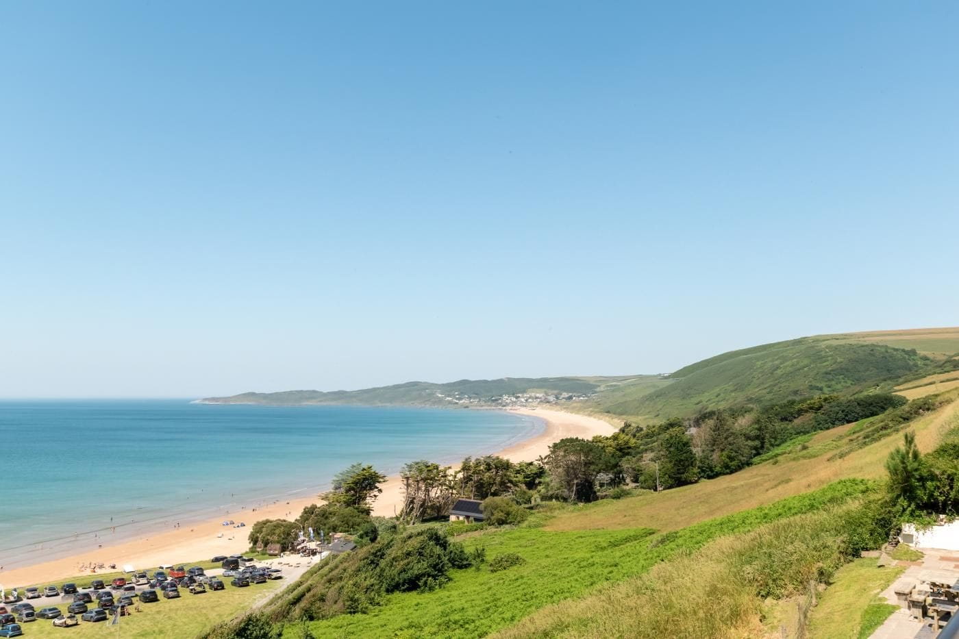 Eine Küstenlandschaft mit Strand, grünen Hügeln und blauem Himmel.
